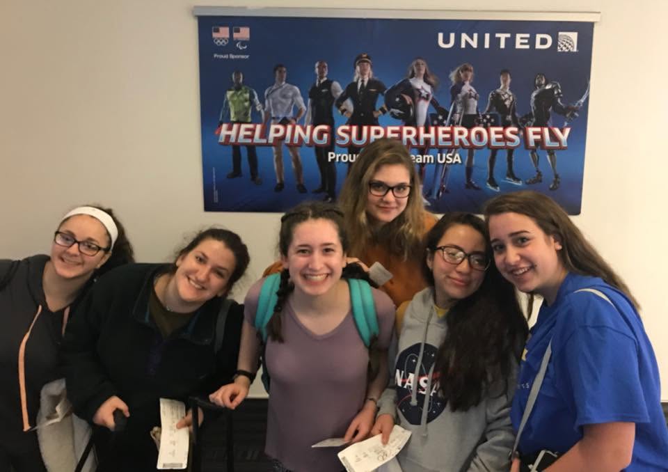 North Shore teen volunteers at the airport beneath United Airlines’ ‘Helping Superheroes Fly’ banner.